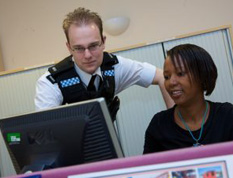 A photograph showing a police officer looking at information on a laptop with a colleague